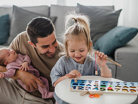 Happy young man taking care of his newborn baby and little daughter indoors at home, paternity leave.